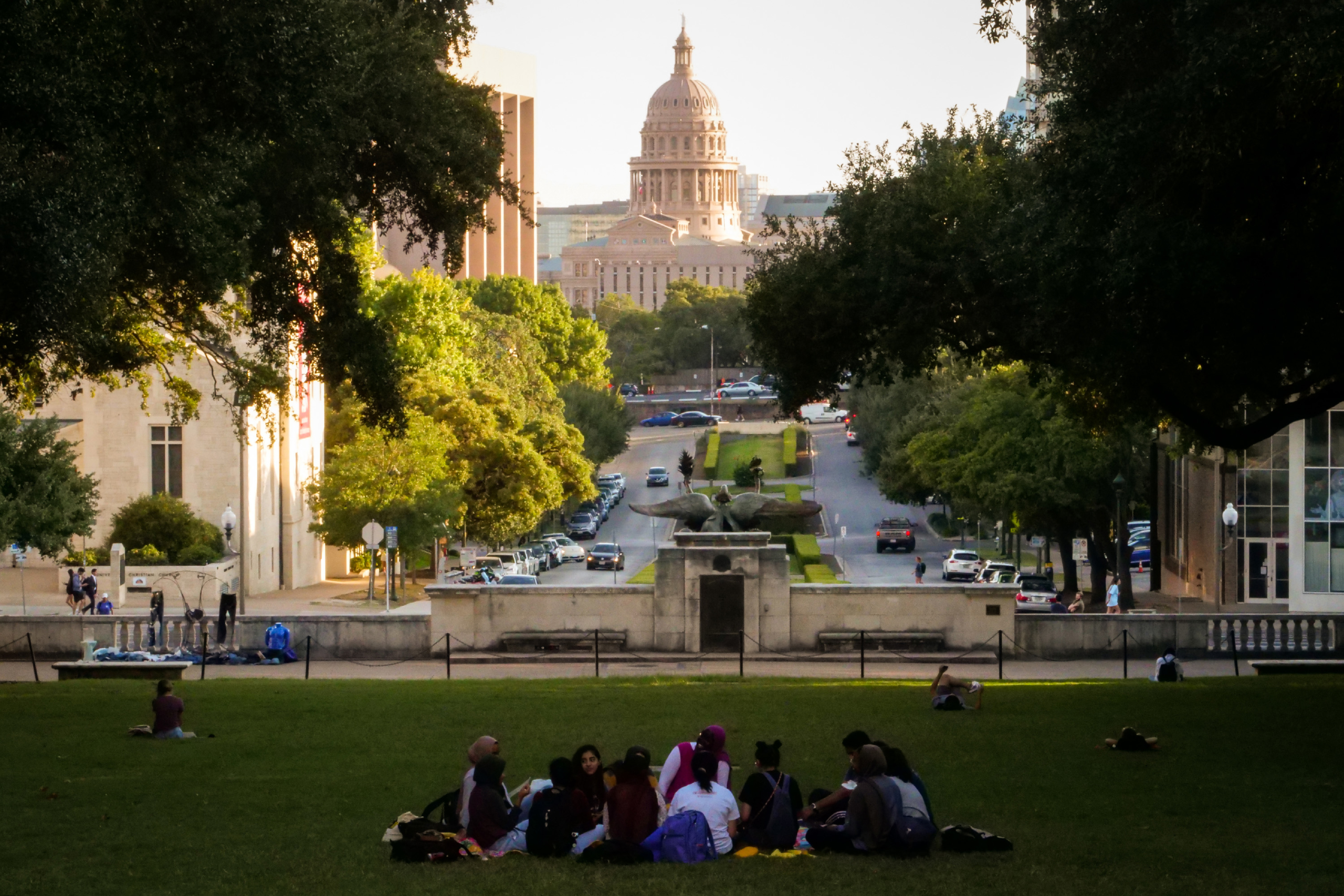 Students sit on the lawn of South Mall at UT-Austin with the Texas State Capitol in the background
