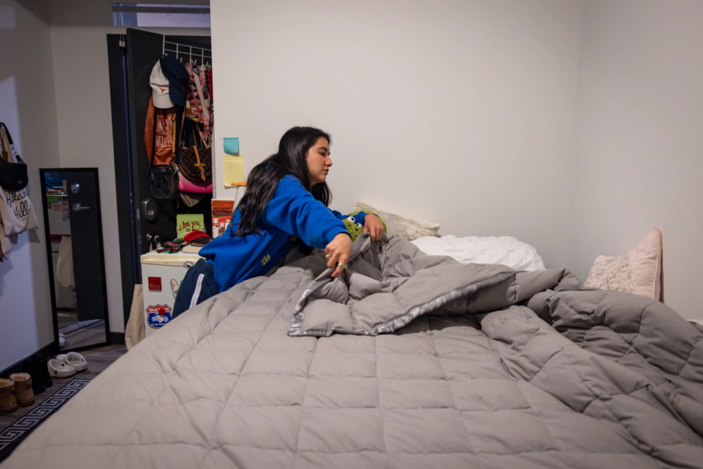 A person adjusts a gray comforter on a bed